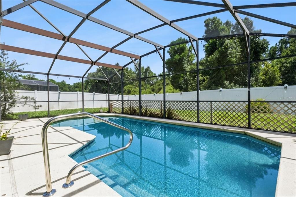 A swimming pool enclosed by a screened lanai with a white privacy fence in the background — 435 SCRUB JAY WAY, DAVENPORT, FL