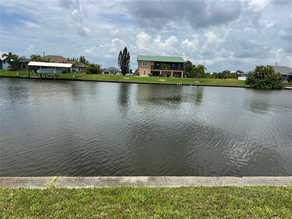 A view across a canal toward a two-story house with a green metal roof — 9272 ARRID CIRCLE, PORT CHARLOTTE, FL