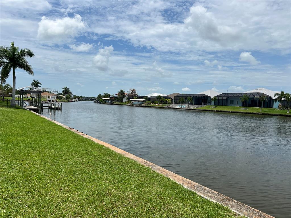 A canal view from a grassy backyard featuring a concrete seawall and residential homes — 9272 ARRID CIRCLE, PORT CHARLOTTE, FL