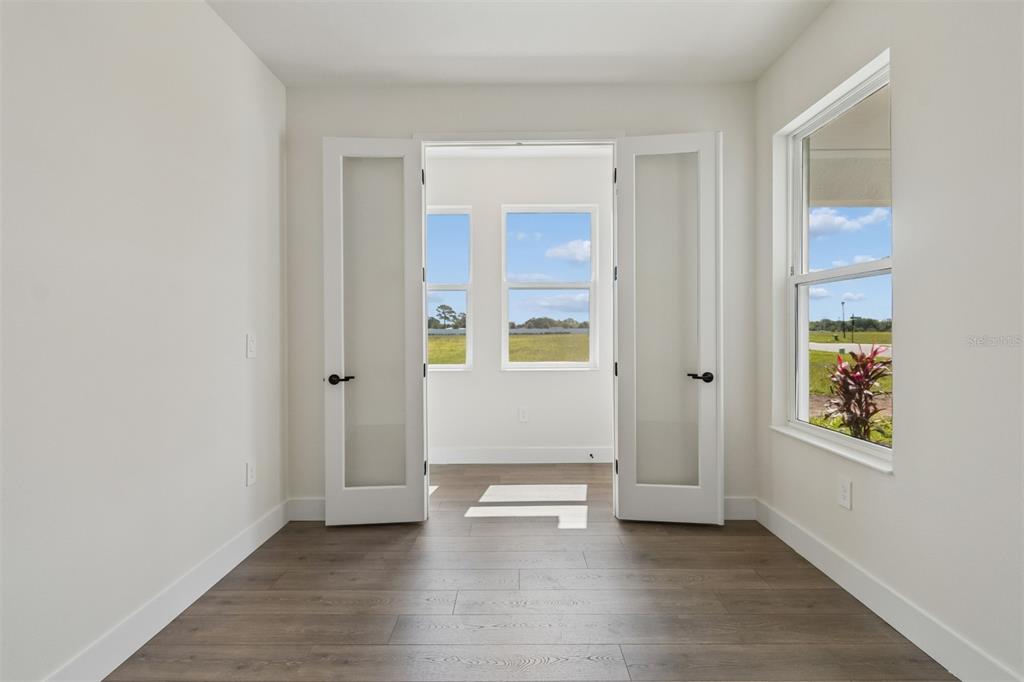 A room with wood-look flooring and French doors opening to a sunroom with water views — 2856 MARRAKESH LANE, SARASOTA, FL