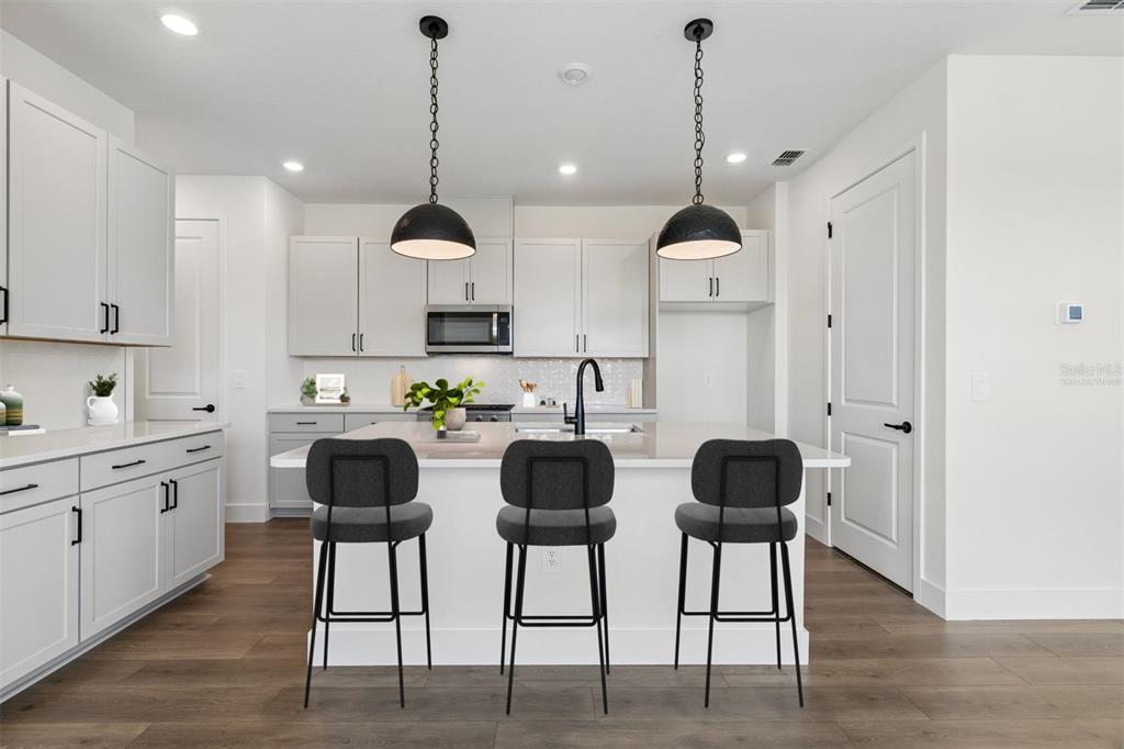 A modern kitchen features white cabinetry, a central island with three stools, and pendant lighting — 2856 MARRAKESH LANE, SARASOTA, FL