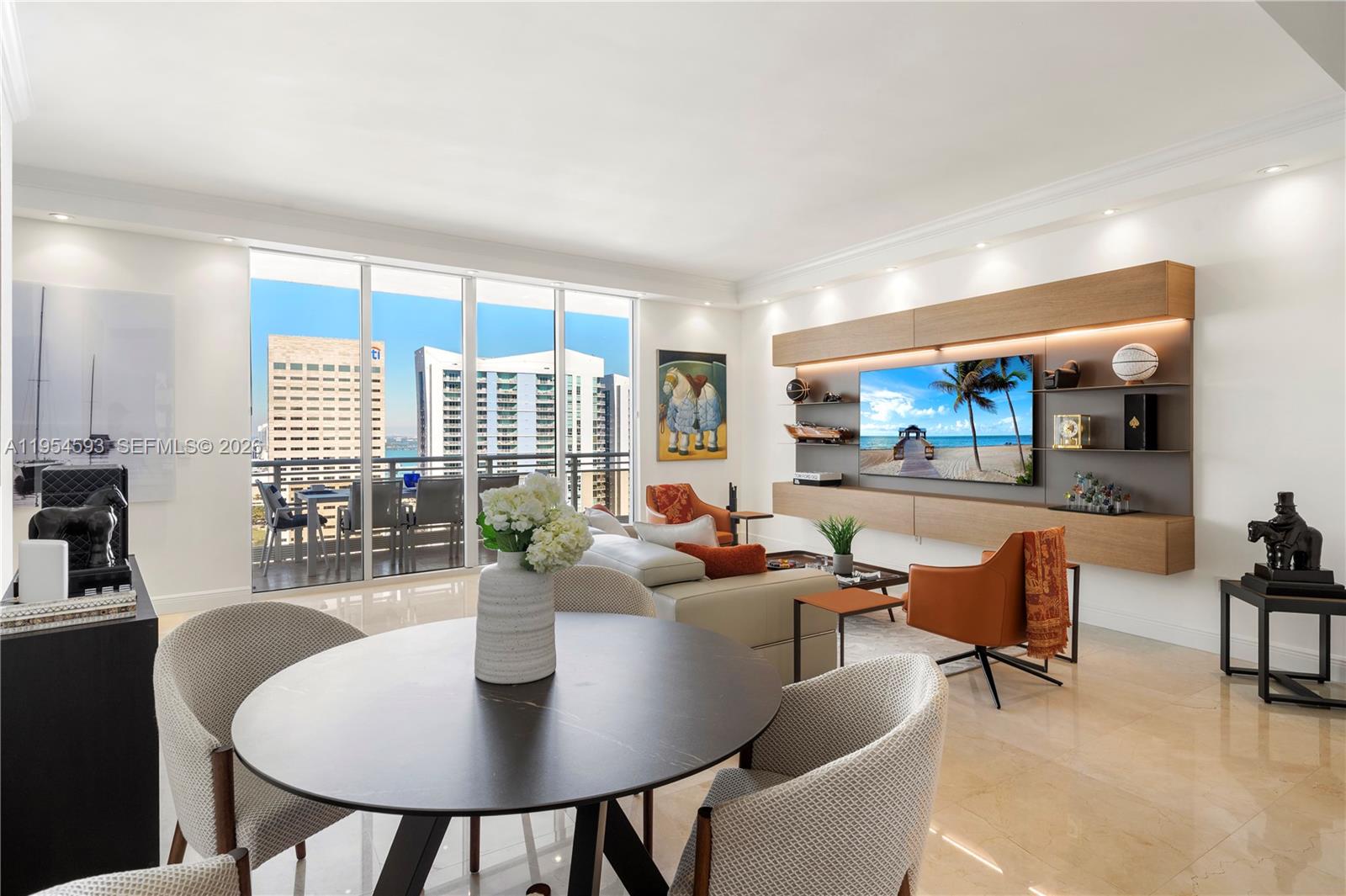 A modern living and dining area features a wall-mounted entertainment unit and balcony views — 901 Brickell Key Blvd # 3706, Miami FL 33131, MIAMI, FL