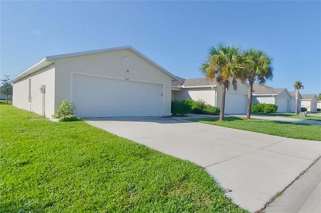 A single-story suburban house with a two-car garage, concrete driveway, and palm trees — 9120 AEGEAN CIRCLE, LEHIGH ACRES, FL