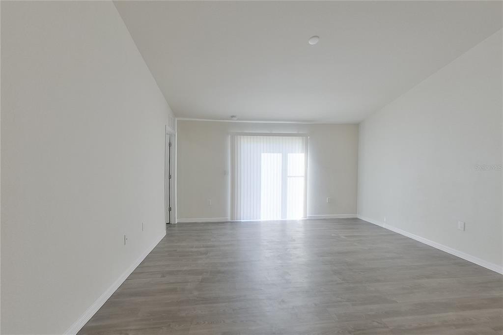 An empty living room features light gray wood-look flooring, white walls, and sliding glass doors — 9120 AEGEAN CIRCLE, LEHIGH ACRES, FL