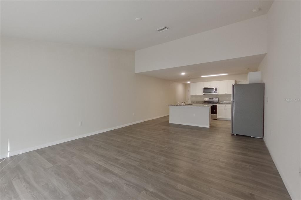 An open-concept living area features light-colored walls, gray wood-look flooring, and a kitchen with white cabinets — 9120 AEGEAN CIRCLE, LEHIGH ACRES, FL