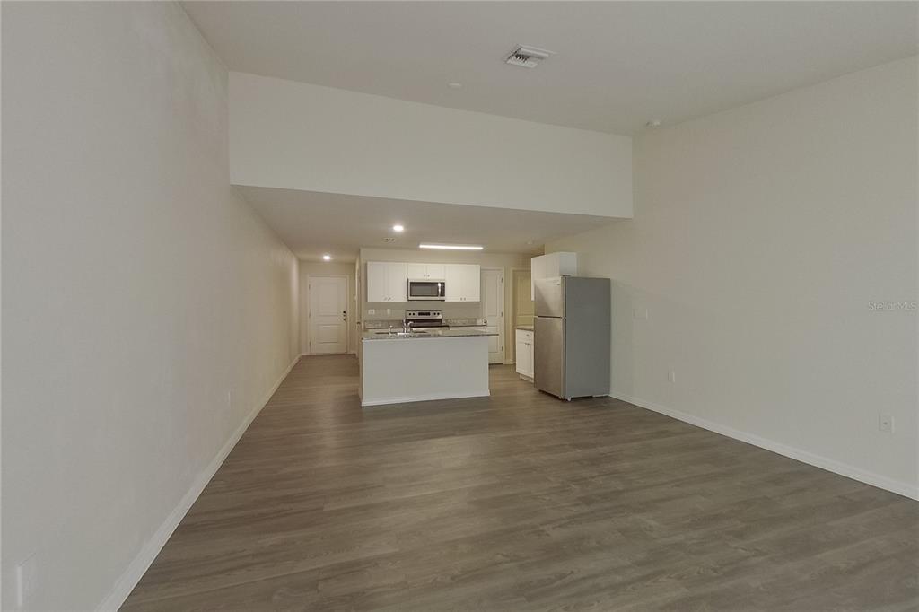 An open-concept kitchen with white cabinets and a stainless steel refrigerator overlooks a living area — 9120 AEGEAN CIRCLE, LEHIGH ACRES, FL