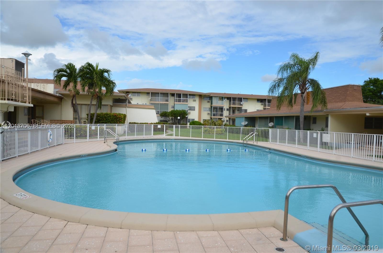 A swimming pool with a white fence is surrounded by multi-story apartment buildings and palm trees — 17090 NE 14th Ave # 312, North Miami Beach FL 33162, NORTH MIAMI BEACH, FL