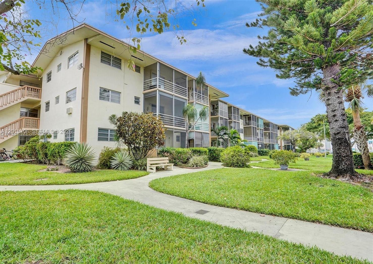 A multi-story apartment building with screened balconies sits behind a landscaped lawn and walkway — 17090 NE 14th Ave # 312, North Miami Beach FL 33162, NORTH MIAMI BEACH, FL