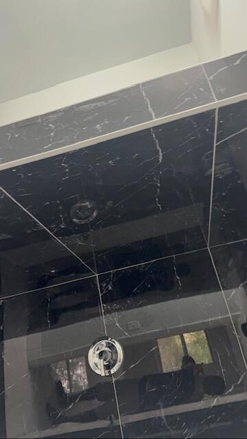 A close-up view of a shower wall featuring black marble-style tiles and a chrome faucet — CORAL SPRINGS, FL