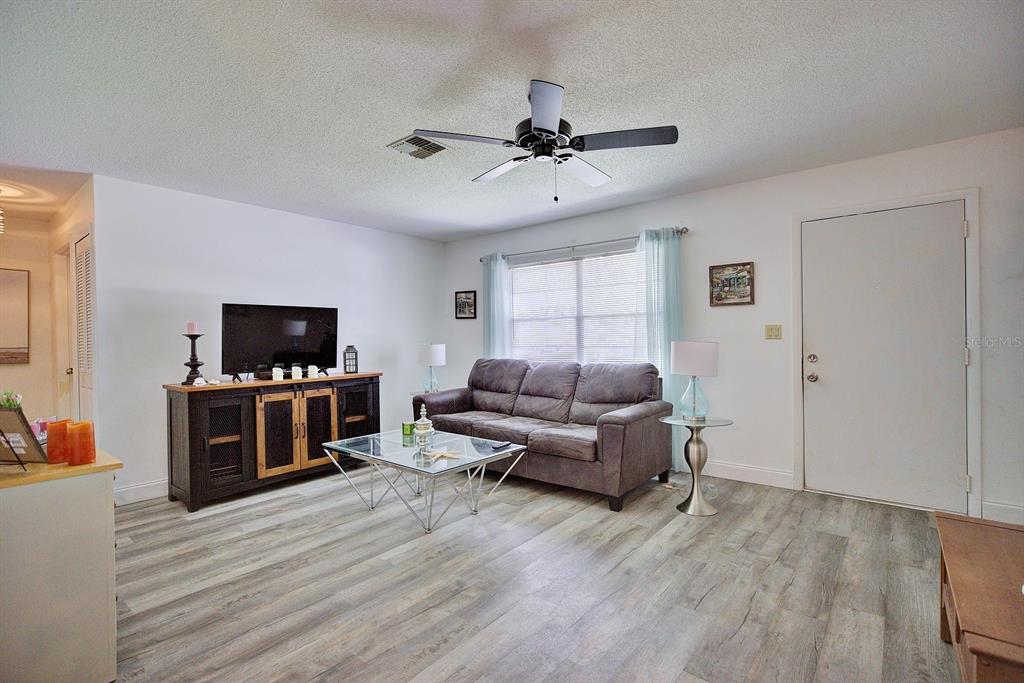 A living room features a grey sofa, a glass coffee table, and wood-look flooring — 306 LARK TERRACE, SEBRING, FL