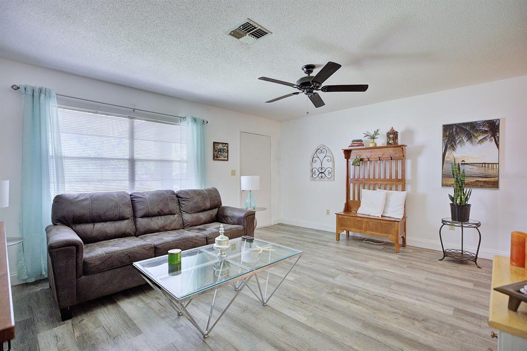 A living room features a dark sofa, glass coffee table, and wood-look flooring — 306 LARK TERRACE, SEBRING, FL