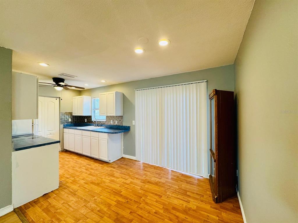 A kitchen with white cabinets, blue countertops, and wood-look flooring opens to a dining area — 12909 LITEWOOD DRIVE, HUDSON, FL