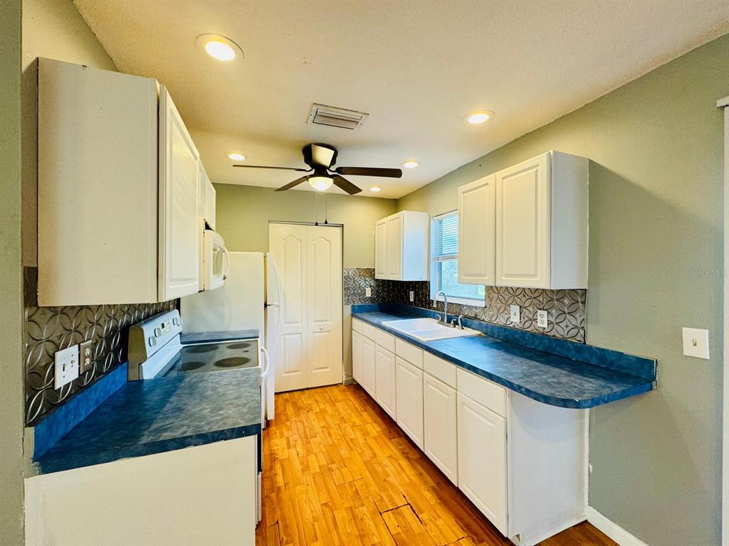 A kitchen features white cabinets, blue countertops, a patterned backsplash, and a ceiling fan — 12909 LITEWOOD DRIVE, HUDSON, FL