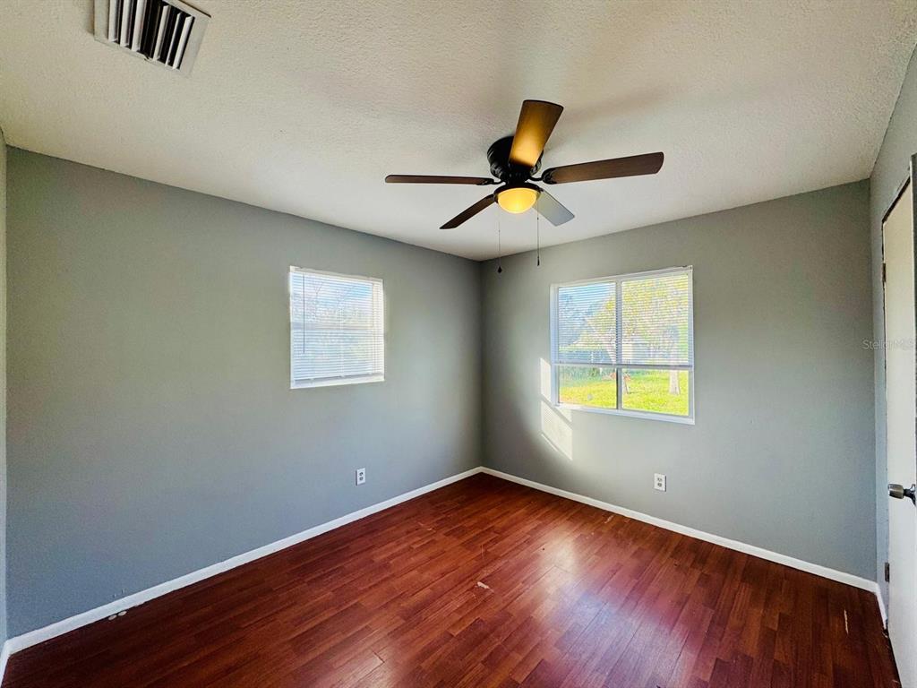 An empty bedroom with gray walls, wood-look flooring, two windows, and a ceiling fan — 12909 LITEWOOD DRIVE, HUDSON, FL