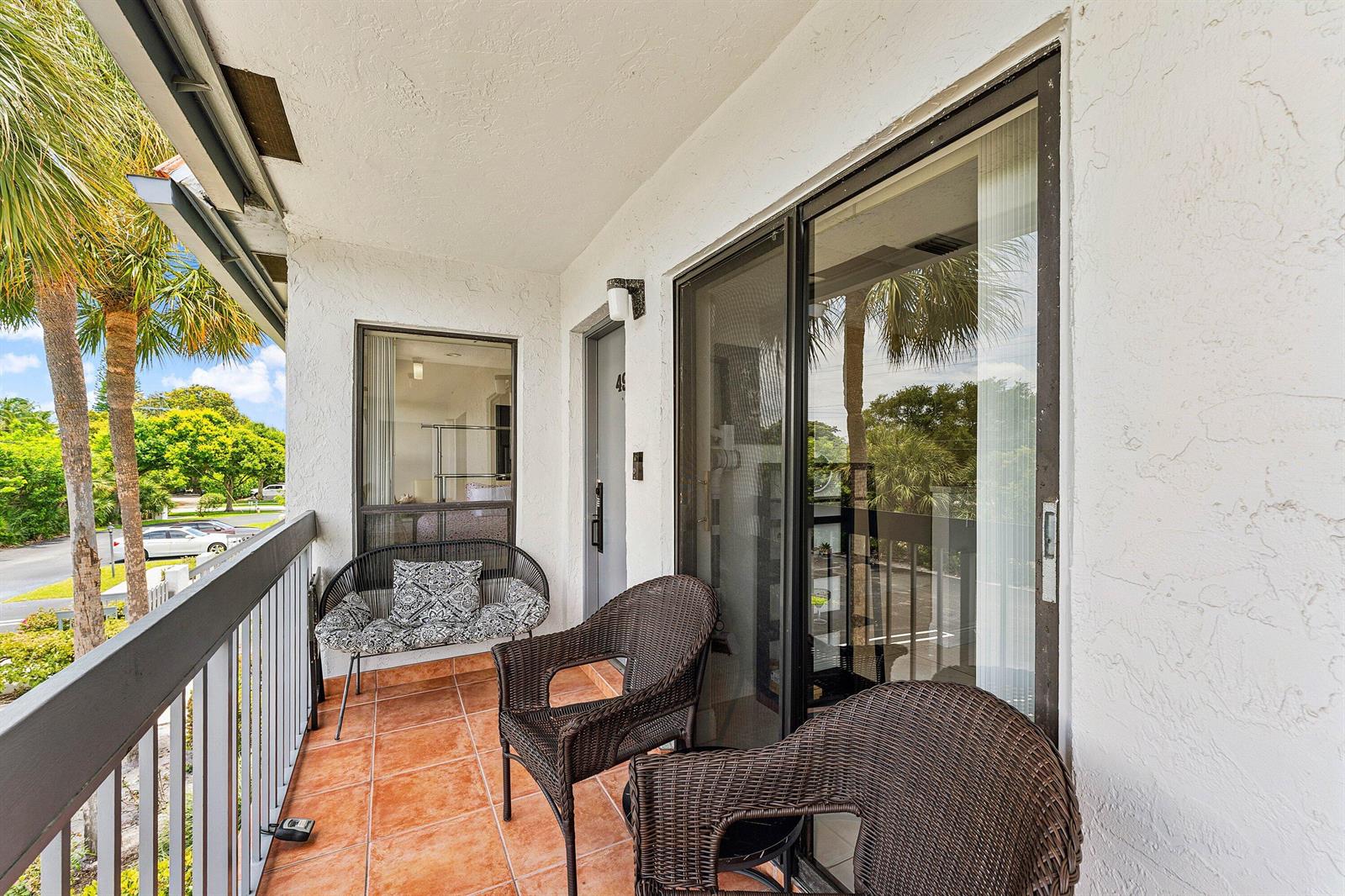 A balcony with tiled flooring, wicker furniture, and a sliding glass door overlooking a parking lot — 3220 Frederick Boulevard # 49u, Delray Beach FL 33483, DELRAY BEACH, FL