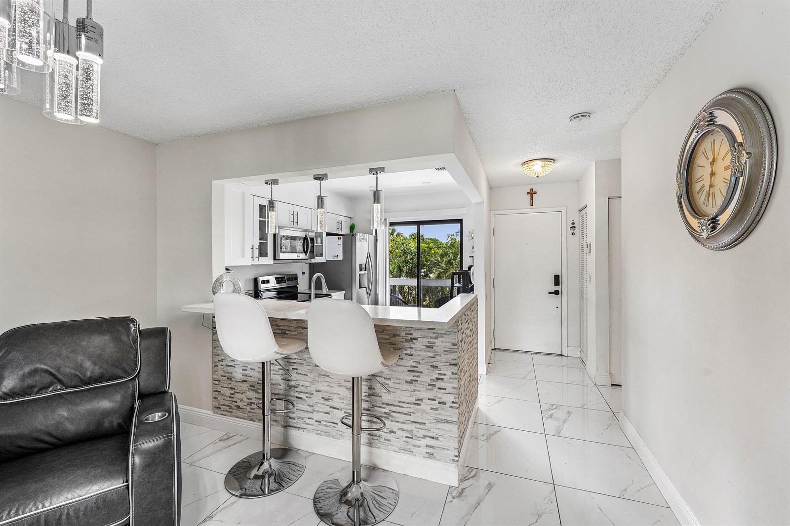 A kitchen with a breakfast bar, white cabinets, and tiled floors opens to a living area — 3220 Frederick Boulevard # 49u, Delray Beach FL 33483, DELRAY BEACH, FL