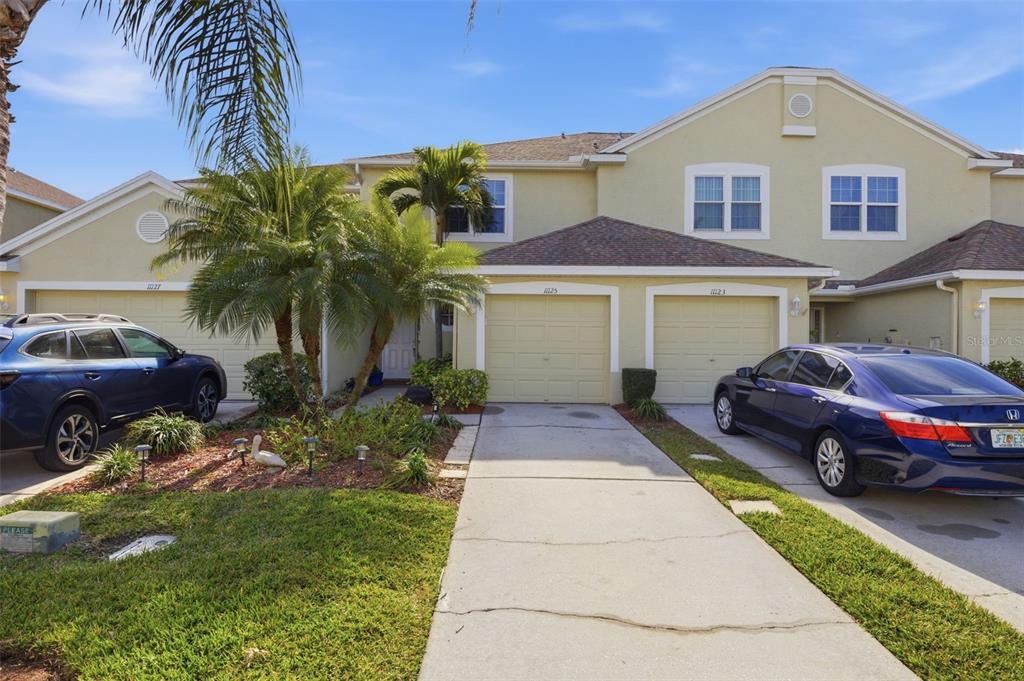 A two-story townhouse exterior with two garage doors, a palm tree, and two parked cars — 11125 KAPOK GRAND CIRCLE, MADEIRA BEACH, FL