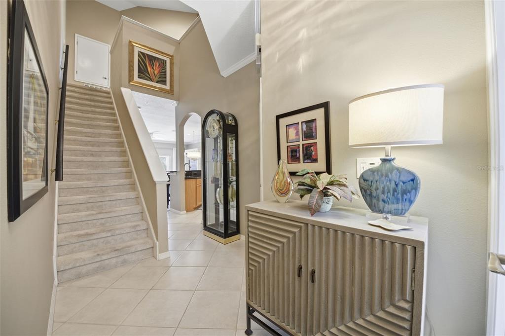 A foyer features a staircase, a decorative cabinet with a lamp, and a tall clock — 11125 KAPOK GRAND CIRCLE, MADEIRA BEACH, FL