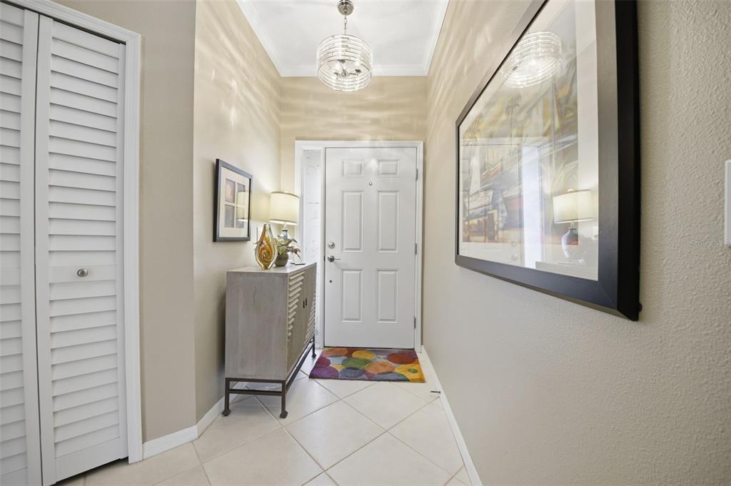 A bright entryway features a white front door, a small cabinet, and a modern chandelier — 11125 KAPOK GRAND CIRCLE, MADEIRA BEACH, FL