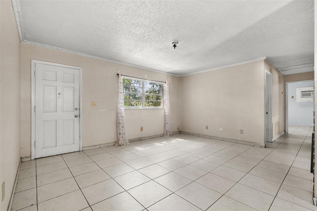 An empty room features beige walls, white tile flooring, a window with curtains, and a door — 3805 S TAMPA AVENUE, ORLANDO, FL
