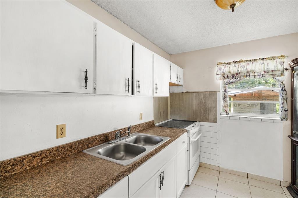 A kitchen features white cabinets, a brown speckled countertop, a double sink, and a stove — 3805 S TAMPA AVENUE, ORLANDO, FL