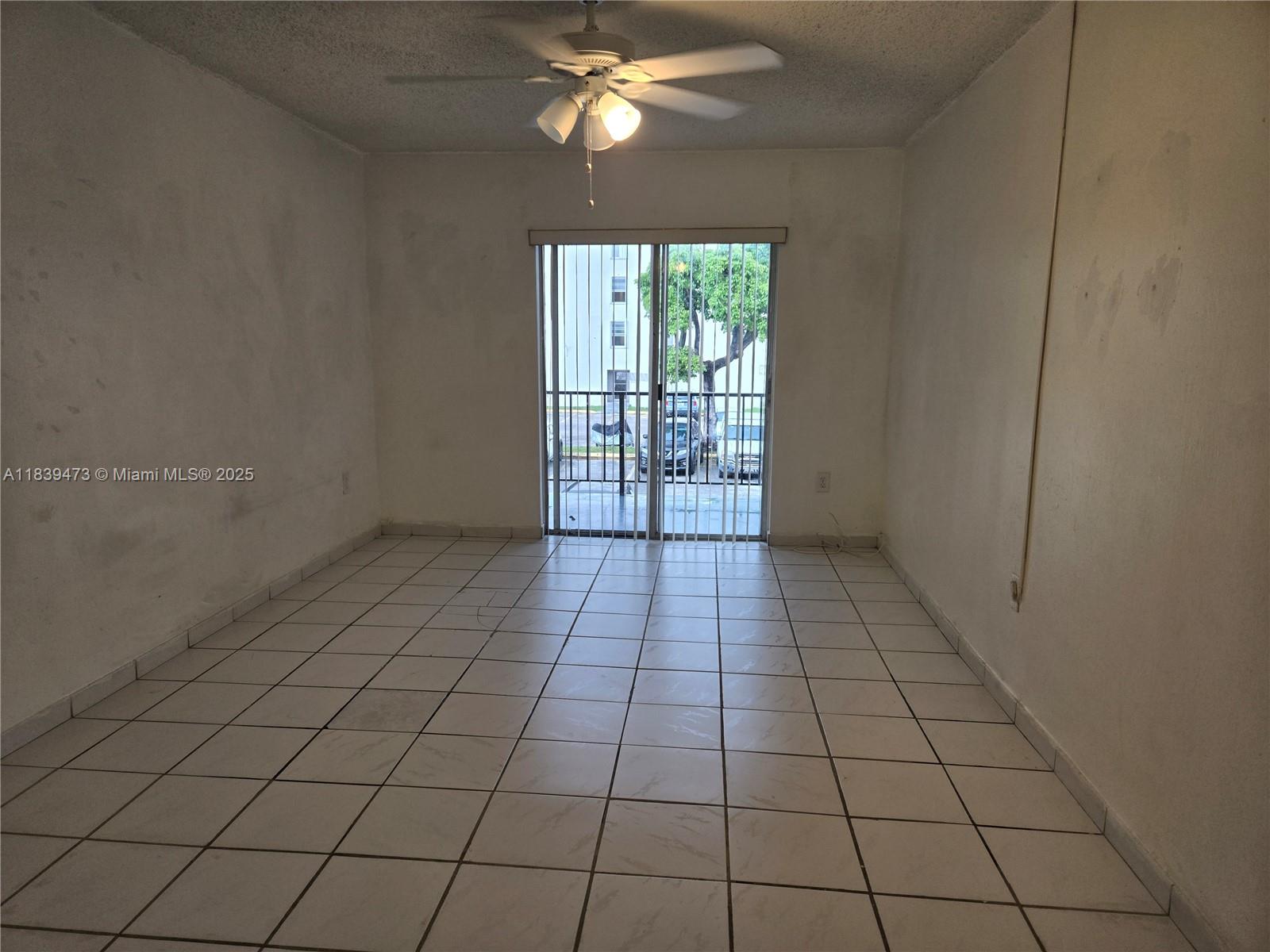 An empty room features white tiled floors, a ceiling fan, and sliding glass balcony doors — 5755 W 20 Ave # 206, Hialeah FL 33012, HIALEAH, FL