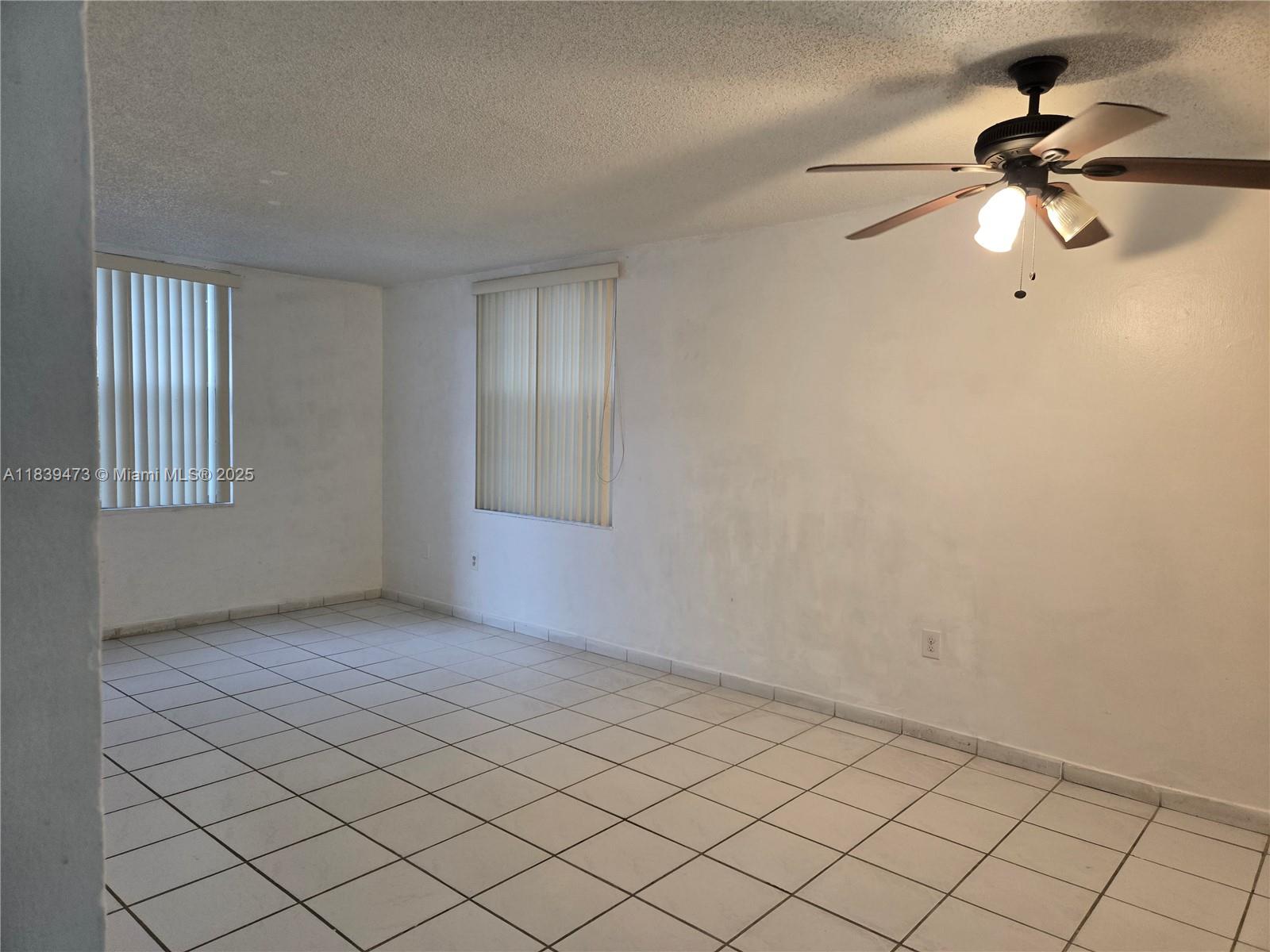 An empty room features white walls, white tile flooring, two windows with blinds, and a ceiling fan — 5755 W 20 Ave # 206, Hialeah FL 33012, HIALEAH, FL