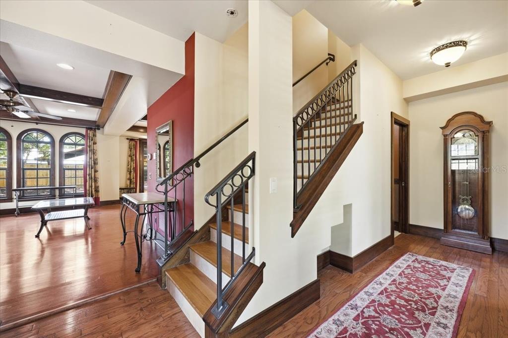 An interior view shows a foyer with a wooden staircase, hardwood floors, and a grandfather clock — 1719 7TH STREET, SARASOTA, FL