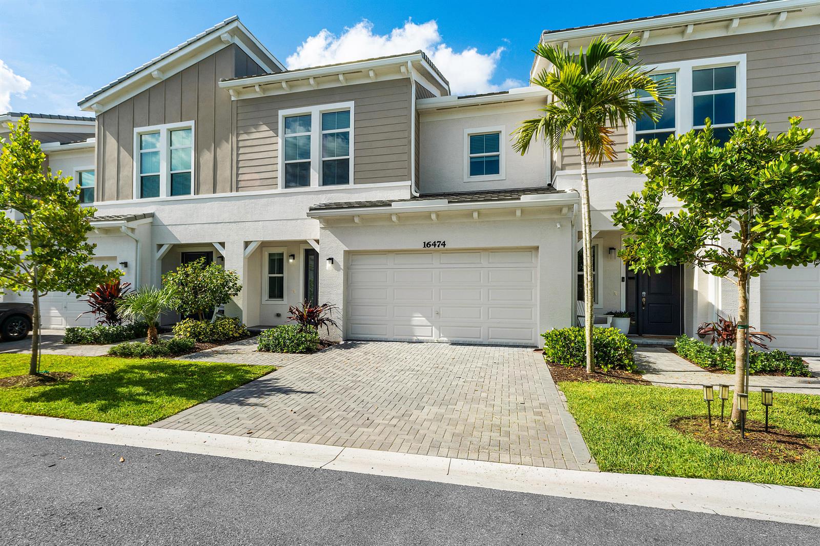 A two-story townhouse with a white garage, paved driveway, and palm trees in the front yard — 16474 Helix Court, FL 33470, FL