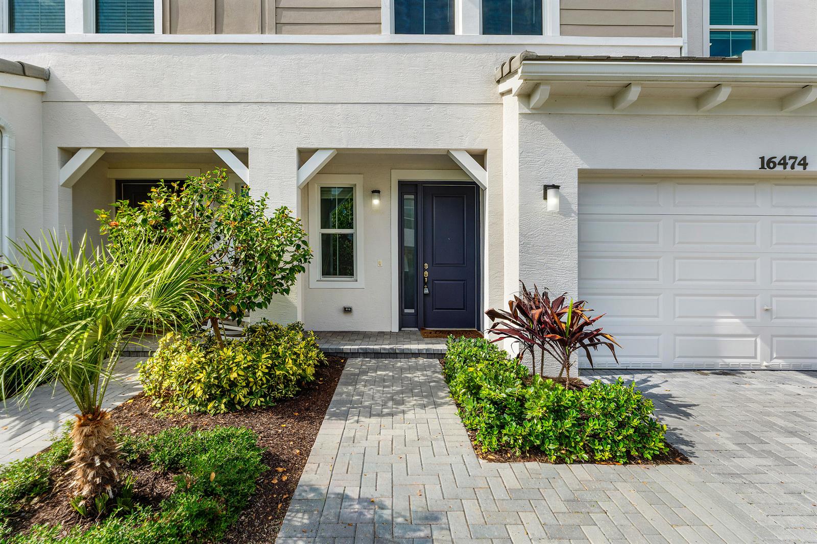 A paved walkway leads to the dark blue front door of a white stucco home — 16474 Helix Court, FL 33470, FL
