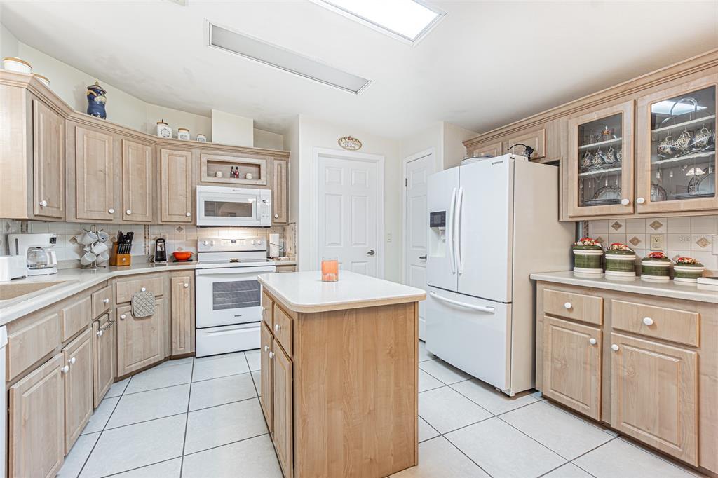 A kitchen with light wood cabinets, white appliances, a center island, and tiled flooring — 37349 GILL AVENUE, ZEPHYRHILLS, FL