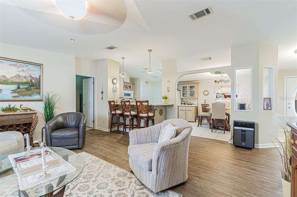 An open-concept living room features wood-look flooring, a kitchen breakfast bar, and a dining area — 37349 GILL AVENUE, ZEPHYRHILLS, FL
