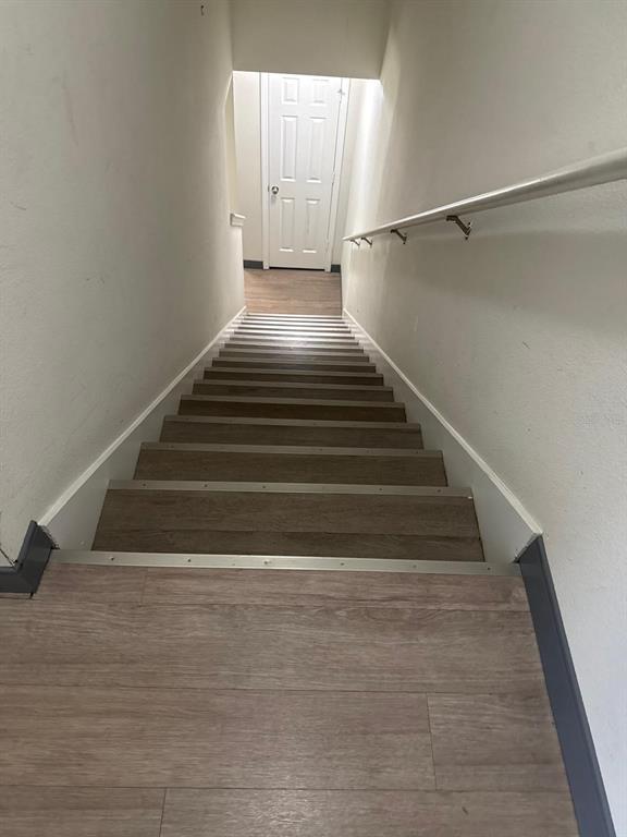 A straight staircase with wood-look flooring and a metal handrail leads to a white door — 4717 CHATTERTON WAY, RIVERVIEW, FL