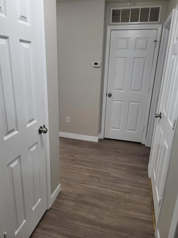 A hallway with wood-look flooring, white doors, and a wall-mounted thermostat — 4717 CHATTERTON WAY, RIVERVIEW, FL