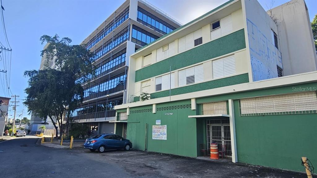 A multi-story green building stands next to a taller modern office building on a street — 10 VELA ST., SAN JUAN, PR