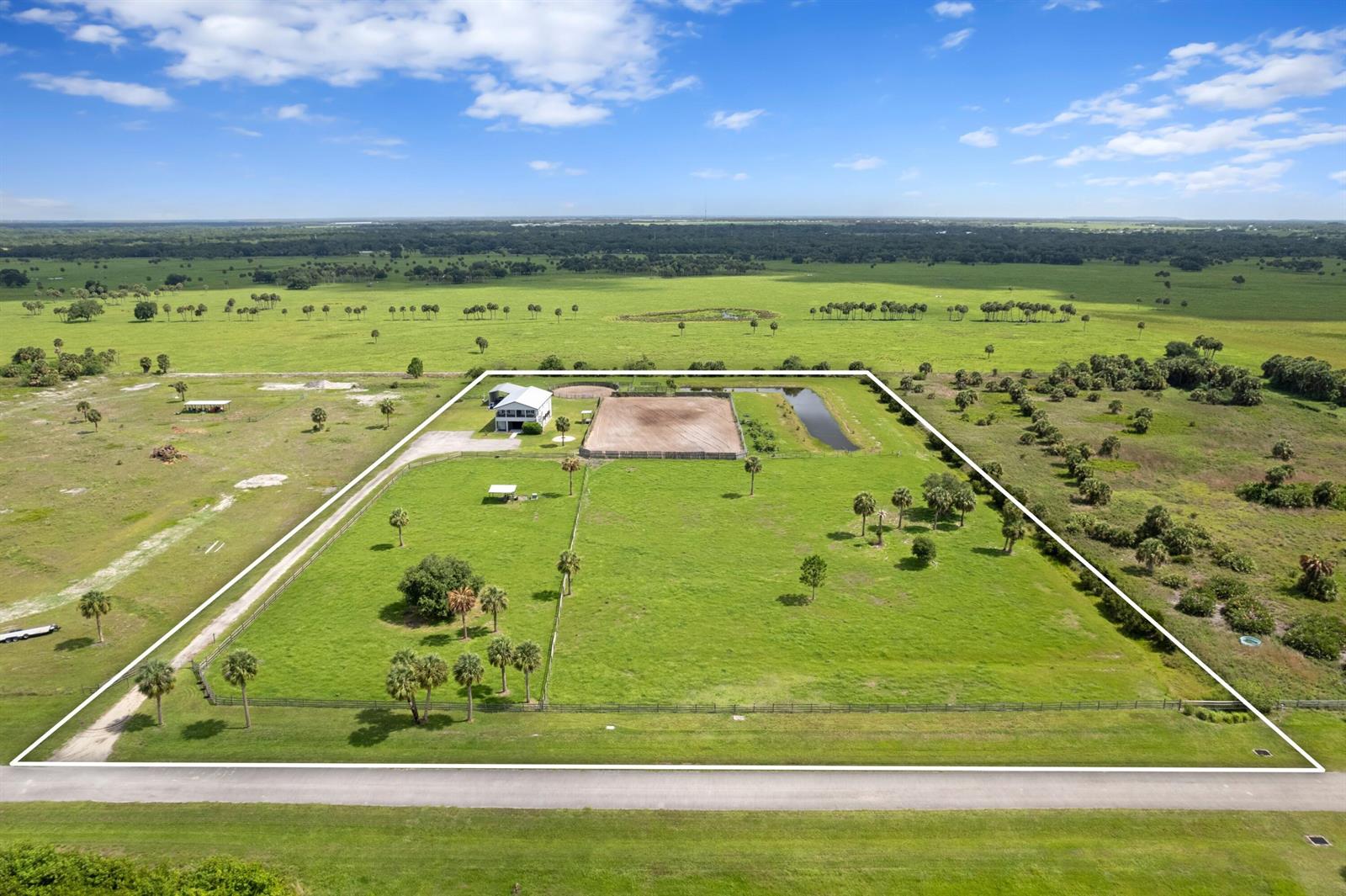 An aerial view shows a fenced rural property featuring a house, riding arena, and pond — 6536 SE 26th Trail, Okeechobee FL 34974, OKEECHOBEE, FL