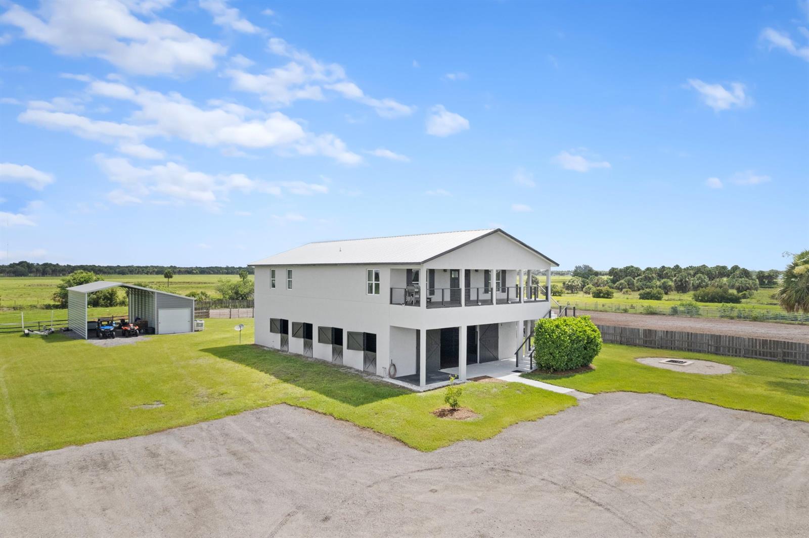 An elevated two-story house with ground-level horse stalls and an adjacent metal carport — 6536 SE 26th Trail, Okeechobee FL 34974, OKEECHOBEE, FL