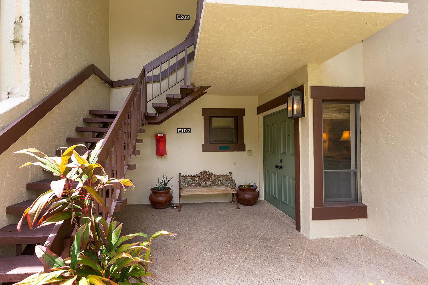 An exterior view of a ground-floor apartment entrance with a staircase, bench, and potted plants — 11397 Pond View Drive # E102, Wellington FL 33414, WELLINGTON, FL