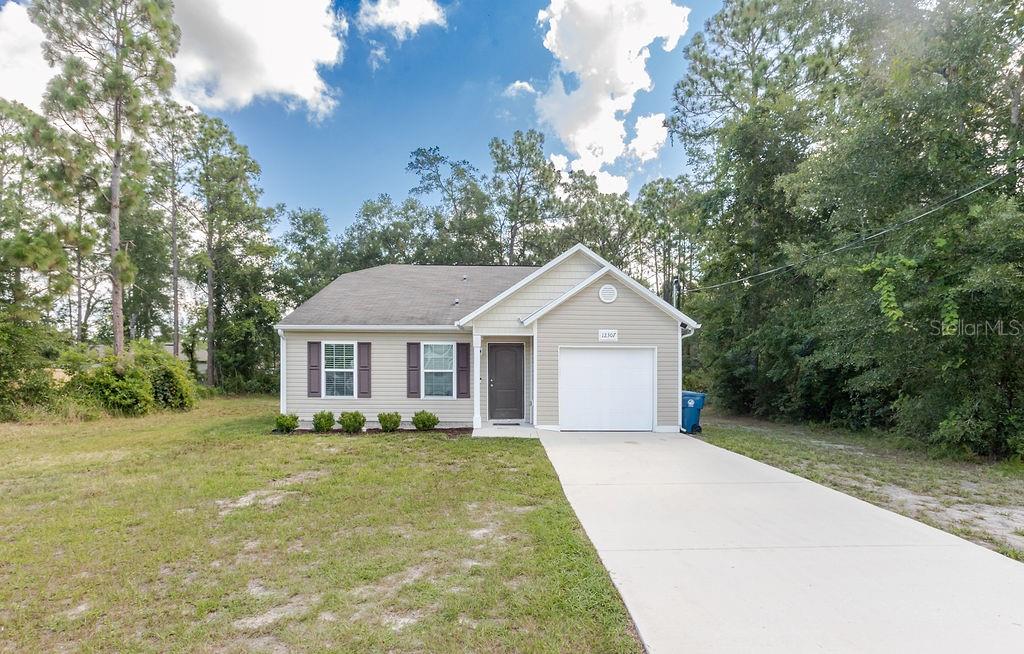 A single-story house with beige siding, a front-facing garage, and a concrete driveway — 12307 MILLINGTON AVENUE, WEEKI WACHEE, FL