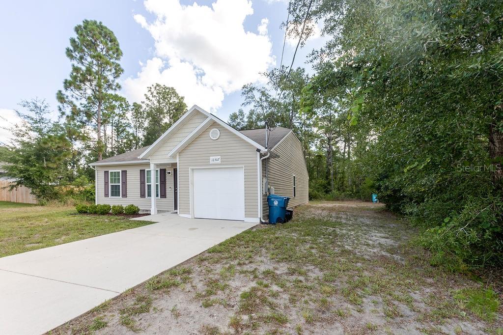 A single-story house with beige siding, a white garage door, and a concrete driveway — 12307 MILLINGTON AVENUE, WEEKI WACHEE, FL