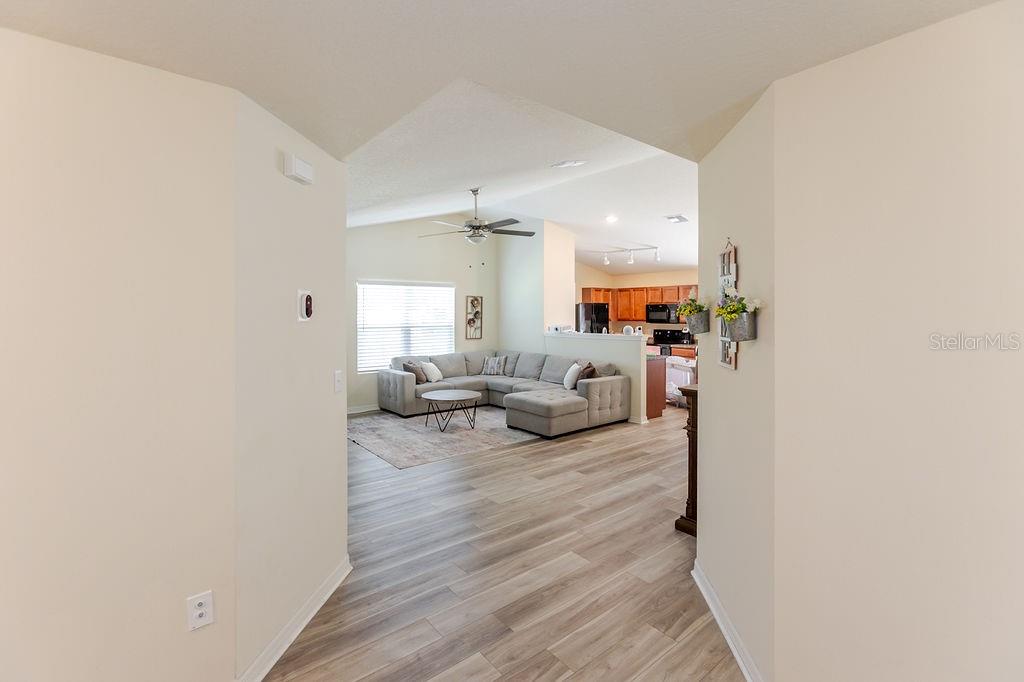 A view from a hallway looking into an open-concept living room with wood-look flooring — 12307 MILLINGTON AVENUE, WEEKI WACHEE, FL