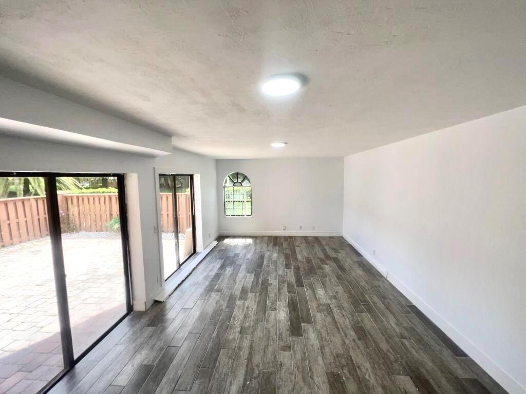 An empty room features wood-look tile flooring, white walls, recessed lighting, and sliding glass doors — 8104 Severn Drive # B, Boca Raton FL 33433, BOCA RATON, FL
