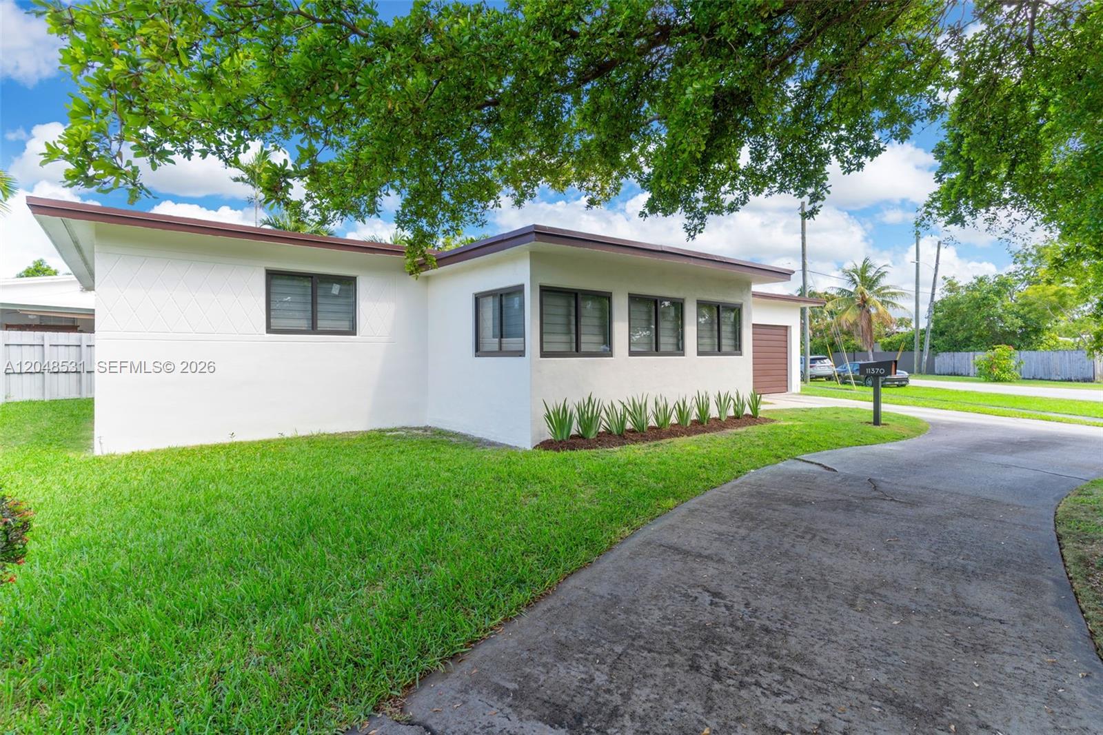 A white single-story house with a flat roof, dark window frames, and a paved driveway — MIAMI, FL