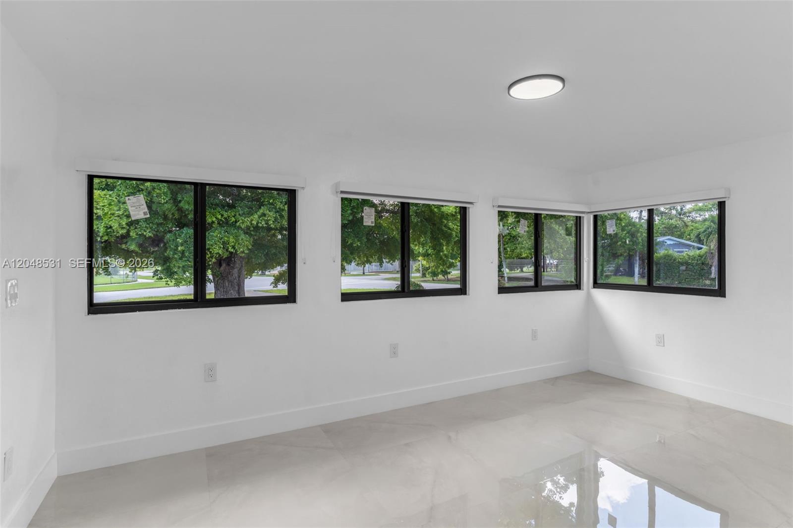 A bright, empty room features white walls, large black-framed windows, and light-colored tile flooring — MIAMI, FL