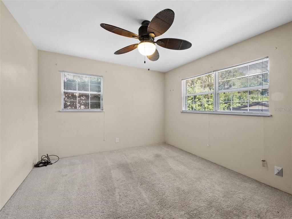 An empty bedroom features beige walls, carpeted flooring, two windows, and a ceiling fan — 25519 COLMAR AVENUE, SORRENTO, FL