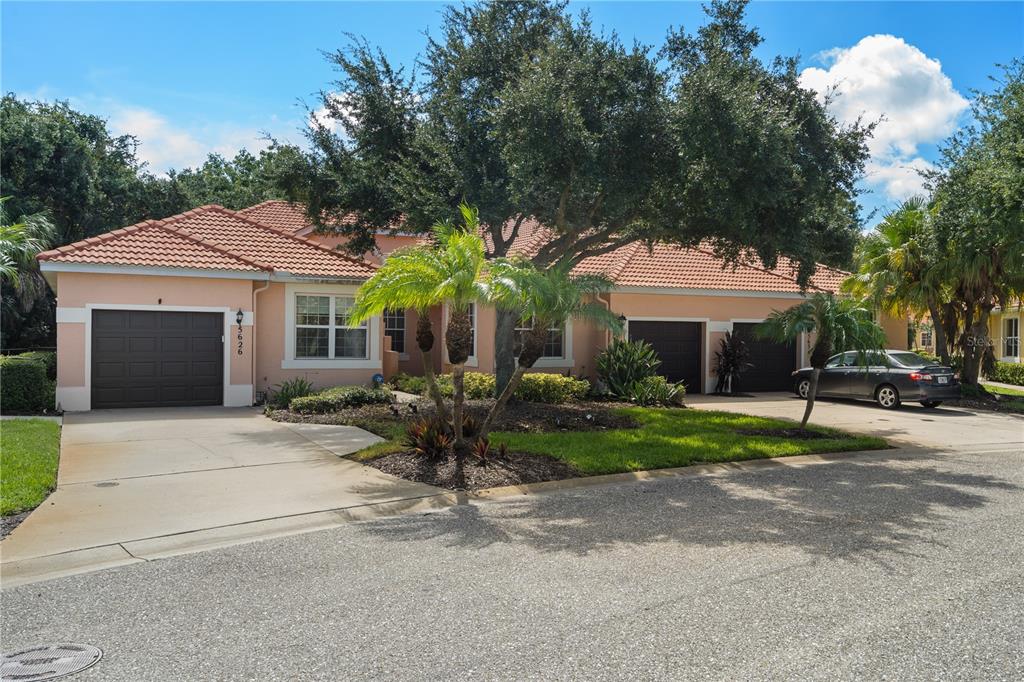 A peach-colored single-story house features a tile roof, three garage doors, and mature landscaping — 5626 CORTINA LANE, PALMETTO, FL