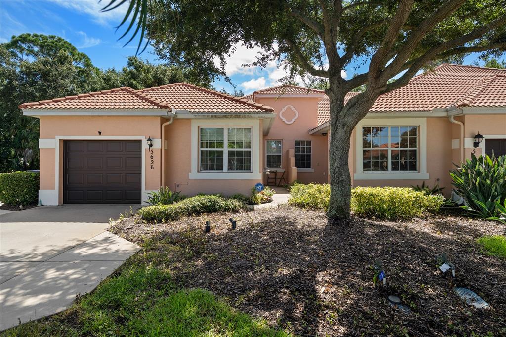 A single-story peach-colored house features a brown garage door, tiled roof, and a large tree — 5626 CORTINA LANE, PALMETTO, FL