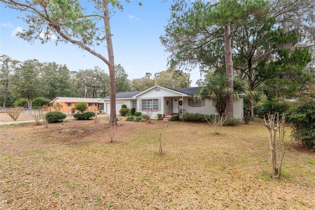 A single-story house with a light-colored exterior sits on a large, tree-filled lot — 3710 NW 22ND PLACE, GAINESVILLE, FL