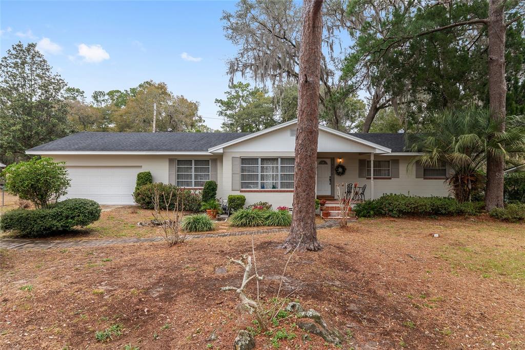 A single-story house with a white exterior, a garage, and a large pine tree in front — 3710 NW 22ND PLACE, GAINESVILLE, FL