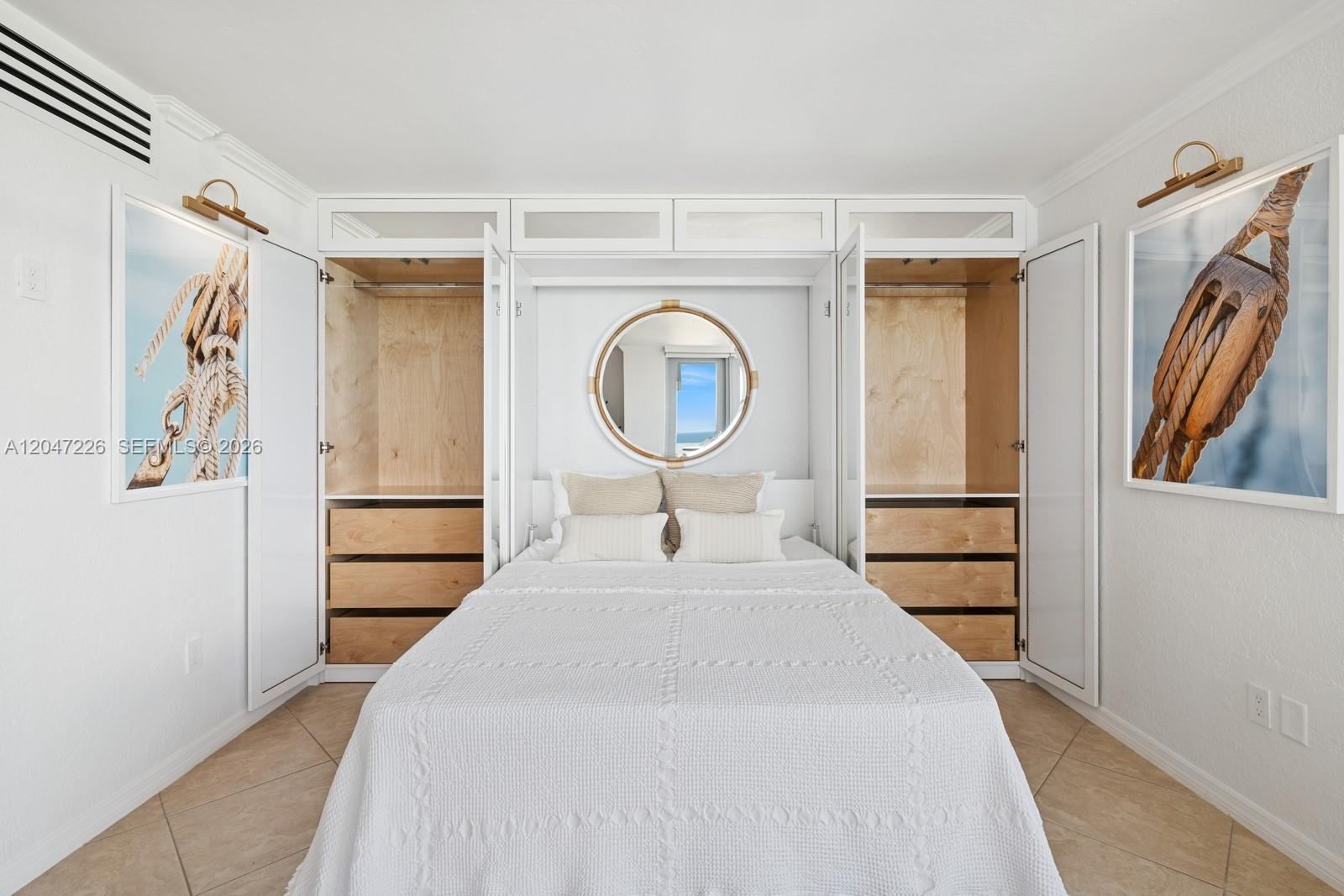 A bedroom features a white Murphy bed flanked by two open wooden closets and wall art — 2899 Collins Ave # 1025, Miami Beach FL 33140, MIAMI BEACH, FL